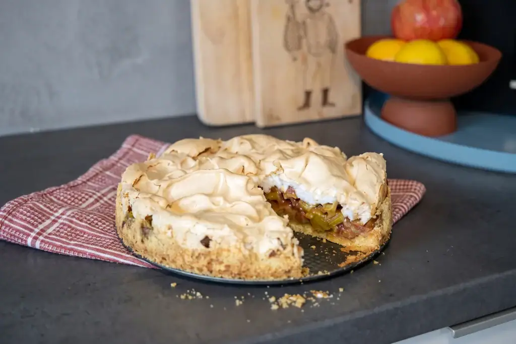 Rhabarberkuchen mit Baiserhaube auf dunklem Küchenarbeitsplatz.